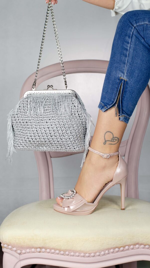 Borsa argento clic clac con frange, lavorata all'uncinetto, con scarpa rosa su una sedia rosa