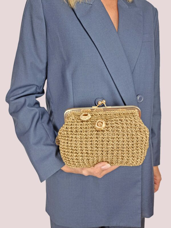 Donna con completo blu che tiene in mano borsa oro con chiusura clic clac, lavorata all'uncinetto.