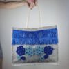 Ragazza con borsa a spalla in tela, con decorazioni azzurre e blu, lavorate all'uncinetto